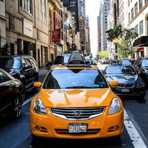 A yellow taxi cab is driving down the street.