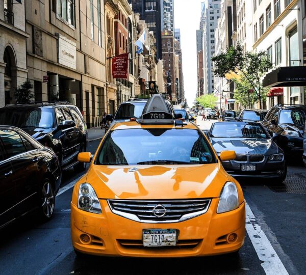 A yellow taxi cab is driving down the street.